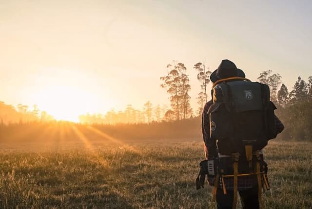 Backpacker watching the sunrise over a misty field at golden hour