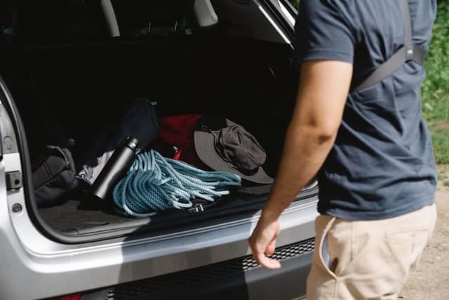 Man loading a rope, water bottle and hat into an open car boot